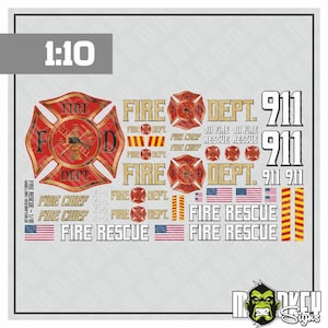 May include: A sheet of 1:10 scale fire department decals featuring red and gold Maltese cross emblems, the text FIRE DEPT, FIRE RESCUE, FIRE CHIEF, and 911, along with small American flag graphics and yellow and red striped hazard warning strips.
