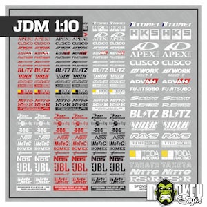 May include: A sheet of 1:10 scale JDM automotive sponsor decals featuring various brand logos in red, black, white, and yellow. The sheet includes multiple rows of text-based stickers such as Apex, Cusco, Work, Advan, Fujitsubo, Spoon, Blitz, Volk, Rays, Top Secret, Toda, Takata, Nitto, RS-R, Fast and Furious, MoTeC, Bomex, NOS, JBL, and Auto Meter.