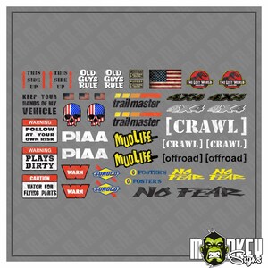 Può includere: Una collezione di adesivi in vinile a tema automobilistico con testi come Old Guys Rule, Trail Master, Mudlife, PIAA, Warn, Sunoco, Foster's e No Fear, insieme a grafiche di bandiere americane, teschi e segnali di avvertimento su sfondo grigio.