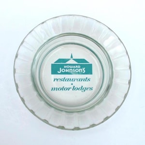 May include: Clear glass ashtray with a ridged edge. The center features the Howard Johnson's logo in teal and white, with the words "restaurants" and "motor lodges".