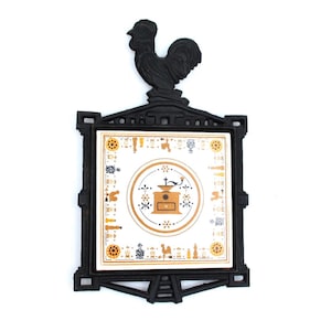 May include: Black cast iron trivet with a rooster on top. The trivet has a square tile insert with a coffee grinder design in the center, surrounded by decorative patterns in gold and blue. A functional and decorative kitchen item.