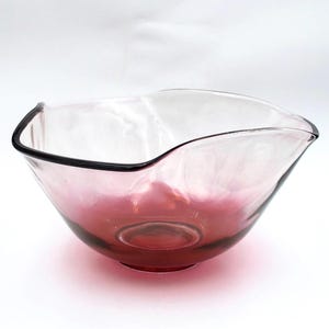 May include: A clear glass bowl with a deep red base that transitions into a lighter pink hue toward the top. The bowl features a distinctively wavy, organic rim with a dark, thin edge, creating a fluid and asymmetrical silhouette.