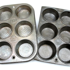May include: Two vintage metal muffin tins. One tin has six round cups with a diamond pattern, the other has six round cups with concentric circles. Both are made of a dull, silver-colored metal and are set against a white background.
