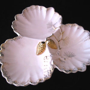 May include: A three-sectioned, white ceramic serving dish with a scalloped edge, accented with gold trim and gold pinecone details. The dish has a delicate, vintage aesthetic, perfect for serving appetizers or small treats.