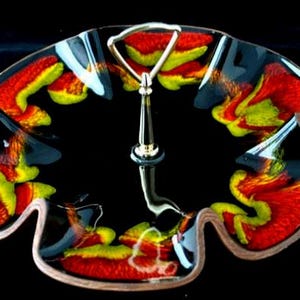 May include: A two-tiered serving dish with a black background. The dish has a gold handle and a wavy, scalloped edge. The dish is decorated with red, yellow, and green abstract designs.