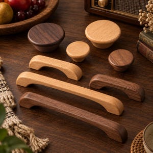 Puede incluir: Una colección de herrajes de madera para muebles que incluye tres pomos redondos y cuatro tiradores de cajón arqueados en tonos de madera clara y oscura. El conjunto presenta bordes suaves y redondeados con vetas de madera natural.