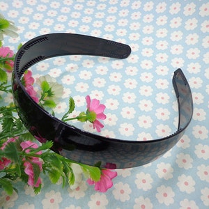 May include: A black plastic headband with a textured surface. The headband is curved and has a smooth, glossy finish.