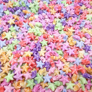 May include: A large assortment of colorful plastic star-shaped beads. The beads are in shades of pink, purple, blue, green, yellow, and orange.