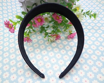 May include: A black headband made of a soft, flexible material. The headband is shown on a light blue background with a white floral pattern.