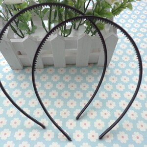 May include: Two black plastic headbands with a textured edge. The headbands are lying on a blue and white floral patterned surface.