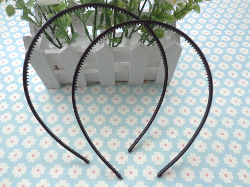 May include: Two black plastic headbands with a textured edge. The headbands are lying on a blue and white floral patterned surface.