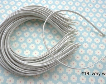 May include: A bundle of ivory white metal headbands, stacked and arranged in a circle on a blue and white floral background. #19 ivory white