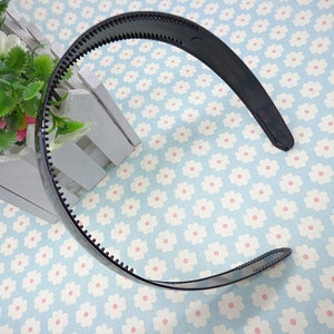 May include: A black plastic headband with a textured edge. The headband is curved and has a smooth, glossy finish.