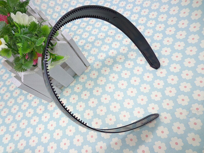 May include: A black plastic headband with a textured edge. The headband is curved and has a smooth, glossy finish.