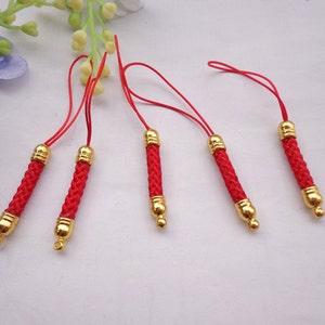 Puede incluir: Cinco charms de teléfono de cordón trenzado rojo y dorado con cuentas doradas en cada extremo. Los cordones están trenzados y tienen un borla en el extremo.