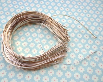 May include: A stack of silver metal headbands, with one headband laid out on a blue and white floral background.
