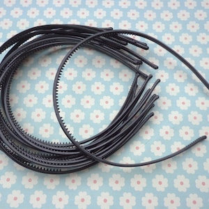 May include: A set of black plastic headbands with a textured edge. The headbands are stacked on top of each other.
