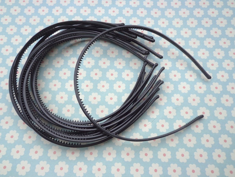May include: A set of black plastic headbands with a textured edge. The headbands are stacked on top of each other.
