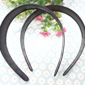May include: Two black plastic headbands with a textured surface. The headbands are curved and have a smooth, rounded edge.