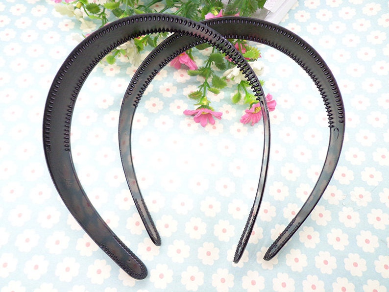 May include: Two black plastic headbands with a textured surface. The headbands are curved and have a smooth, rounded edge.
