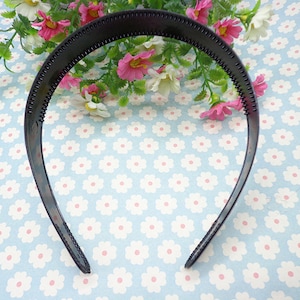 May include: A black plastic headband with a textured surface. The headband is designed to hold hair in place.