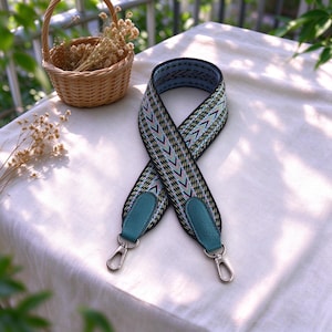 Puede incluir: Una correa de bolso ancha y ajustable con un patrón de chevrón tejido en tonos negro, verde azulado, rosa y amarillo. Los extremos de la correa tienen pestañas de cuero verde azulado texturizado y cierres de mosquetón giratorios de metal plateado.
