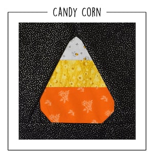 May include: A fabric quilt block featuring a candy corn shape centered on a black background with white speckles. The candy corn is composed of three horizontal sections: a white top with floral patterns, a yellow middle, and an orange base.