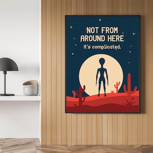 May include: A framed wall art print featuring a dark blue night sky with stars, a large pale yellow moon, and a red desert landscape with cacti. A black alien silhouette stands in the center. The text reads: NOT FROM AROUND HERE It's complicated.