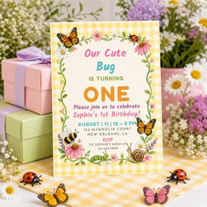 Può includere: Un invito di compleanno rettangolare con bordo a quadretti vichy gialli e bianchi, decorato con illustrazioni di farfalle, una coccinella, un'ape, un bruco e una lumaca. Il testo recita: Our Cute Bug IS TURNING ONE Please join us to celebrate Sophie's 1st Birthday! AUGUST | 11 | 12 – 2 PM 123 MAGNOLIA COURT NEW ORLEANS, LA RSVP TO SOPHIE'S MOM AT 123.456.7890.