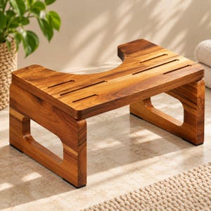 May include: A wooden toilet stool featuring a natural brown grain finish, a curved cutout design, and horizontal ventilation slots on the top surface. The stool is supported by two sturdy side panels with open rectangular cutouts.