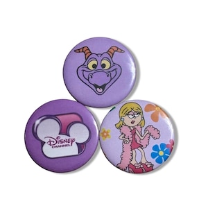 May include: Three circular pin-back buttons featuring Disney Channel imagery. One button displays the purple dragon Figment, another shows the Disney Channel logo, and the third depicts a blonde character with a pink boa and flowers.