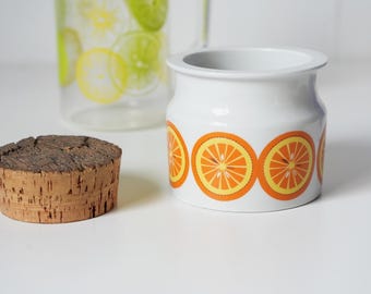 May include: White ceramic jar with a cork lid and a repeating pattern of orange slices. The jar is decorated with a white background and orange slices.