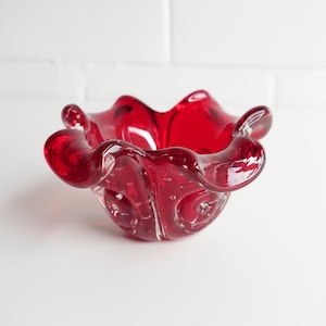 May include: A striking red glass bowl with a unique, ruffled design. The bowl features a bubbly texture and a glossy finish, enhancing its visual appeal. The bowl's shape is reminiscent of a flower.