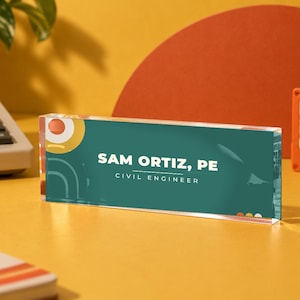 Könnte beinhalten: Ein rechteckiges Schreibtisch-Namensschild aus klarem Acryl mit dunkelblaugrünem Hintergrund und weißem Text, der SAM ORTIZ, PE und CIVIL ENGINEER lautet. Das Design enthält abstrakte gelbe und weiße kreisförmige und lineare grafische Akzente.