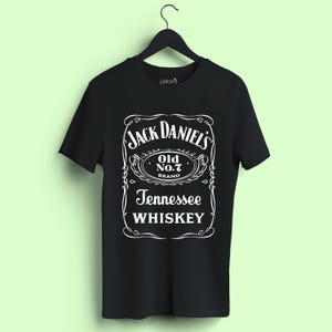 May include: A black short-sleeved t-shirt featuring a white graphic print on the front. The design mimics a Jack Daniel's Tennessee Whiskey label, including the text "Jack Daniel's Old No. 7 Brand Tennessee Whiskey" enclosed in a decorative border.