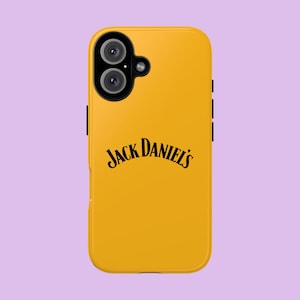 Può includere: Una custodia per smartphone color giallo senape con un modulo fotocamera nero dotato di due lenti circolari e un piccolo flash. Il testo Jack Daniel's è stampato in nero con un carattere curvo e stilizzato al centro del retro della custodia.