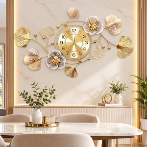 May include: A large wall clock featuring a central circular gold face with black numerals and hands, surrounded by an asymmetrical metal arrangement of gold ginkgo leaves and layered silver and gold floral accents with small gold spheres.
