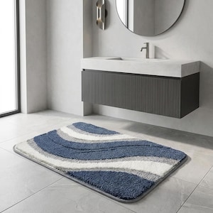 May include: A rectangular bath mat featuring a wavy, multi-textured pattern in shades of navy blue, light gray, and white. The rug has a thick, plush pile construction with distinct curved bands of color that create a flowing, layered visual effect.