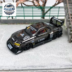 Op de afbeelding: Een zwart 1:64 schaalmodel van een Nissan Skyline met een brede bodykit, een grote achtervleugel en gele koplampen. De buitenkant is versierd met witte race-stickers, waaronder de tekst LBWK, BRIDE en het nummer 5 op de motorkap en deuren.