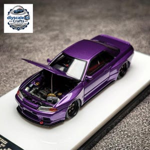Könnte beinhalten: Ein metallisch violettes Modellauto im Maßstab 1:64 mit geöffneter Motorhaube, die Motordetails freigibt, schwarzen Rädern und einer Abschleppöse an der Frontstoßstange. Das Logo diyscale64 Crafts Premium 1:64 Model Cars ist zu sehen.