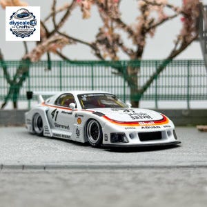 Puede incluir: Un coche de carreras a escala 1:64 de color blanco con el número 41, ruedas negras y varias pegatinas de patrocinadores como Shell, Bosch y Advan. El vehículo cuenta con un kit de carrocería ancho, un alerón trasero y franjas de carreras.
