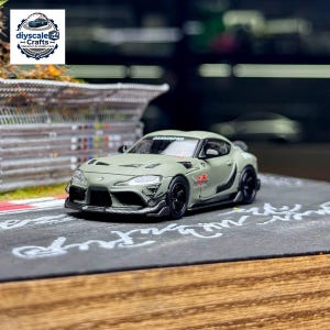 Può includere: Un modellino di auto sportiva in metallo pressofuso verde oliva opaco con ruote nere, uno splitter anteriore in stile fibra di carbonio e decalcomanie grafiche rosse sul lato. Il parabrezza mostra il testo "DARNINPRO" in lettere bianche.