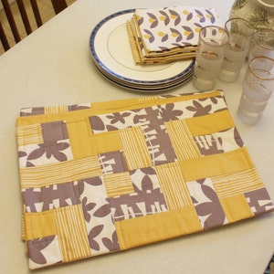 May include: A yellow and gray patchwork table runner with a geometric pattern. The runner is made of fabric squares sewn together.