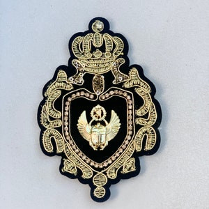 May include: A black velvet embroidered patch with a gold crown, a heart-shaped shield with a gold scarab beetle, and gold embellishments.