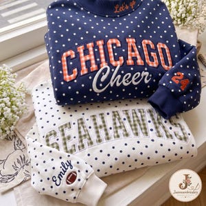 Peut inclure: Un sweat-shirt bleu marine à pois blancs, avec le texte CHICAGO Cheer en appliqué vichy orange et le nombre 24 sur la manche. En dessous, un sweat-shirt blanc à pois bleu marine, avec le texte SEAHAWKS en vichy vert et Emily brodé sur la manche.
