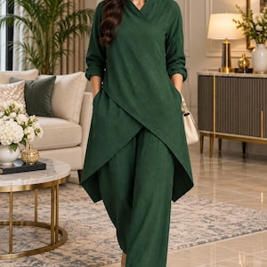 Op de afbeelding: Een donkergroene tweedelige set bestaande uit een tuniek met lange mouwen met een overslag aan de voorzijde, een V-hals en zijzakken, gecombineerd met een bijpassende wijde broek. De tuniek heeft een asymmetrische zoom die aan de voorzijde korter is.