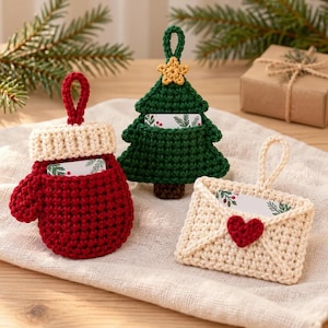 May include: Three crocheted ornaments featuring a red mitten with a cream cuff, a green Christmas tree with a yellow star, and a cream envelope with a red heart. Each piece has a hanging loop and a small card tucked inside the pocket.