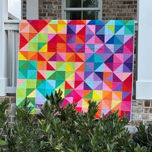 May include: A large rectangular quilt featuring a vibrant geometric pattern composed of numerous multicolored triangles. The design displays a spectrum of bright hues including red, orange, yellow, green, blue, purple, and pink arranged in a grid.