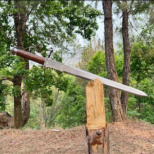 Peut inclure: Une épée en acier à double tranchant dotée d'une longue lame effilée et d'une garde transversale. Le manche est en bois brun foncé avec une gravure géométrique en losange, terminé par un pommeau métallique à la base de la poignée.