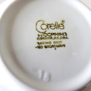 May include: A white ceramic bowl with a gold "Corelle" logo and the text "by Corning, Corning, NY, USA.  Oven Only - No Microwave."  The number "18" is printed on the bottom of the bowl.